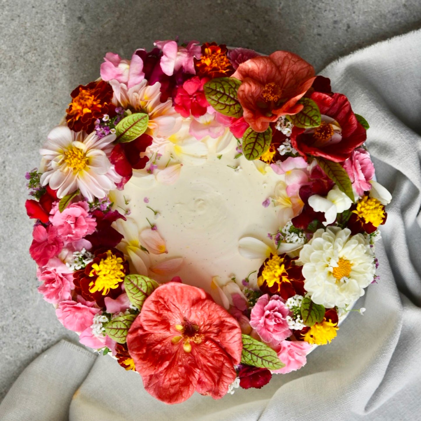 A cake decorated with many different shades of pink edible flowers is pictured from above