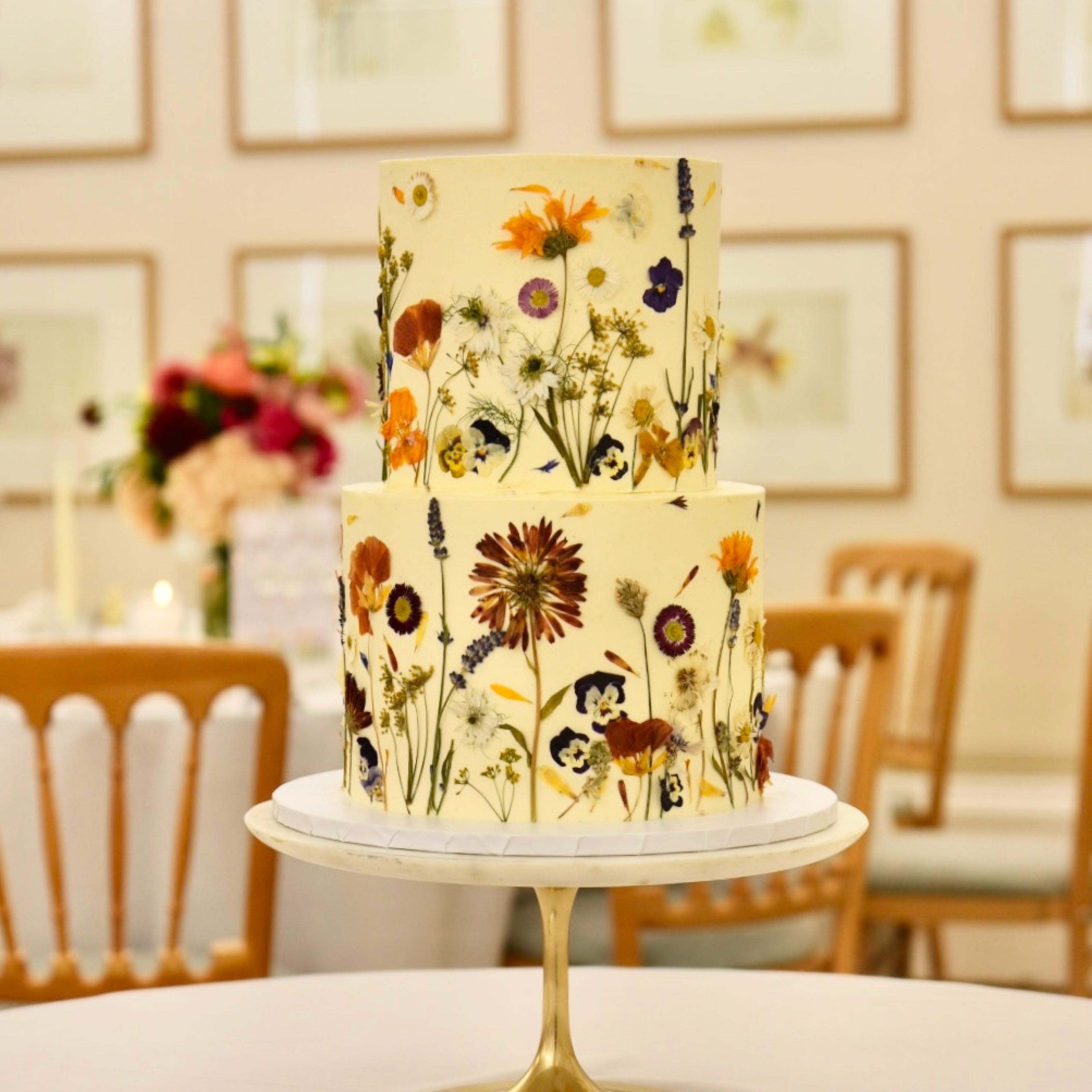 A wedding cake decorated with edible flowers sits on a marble cake stand