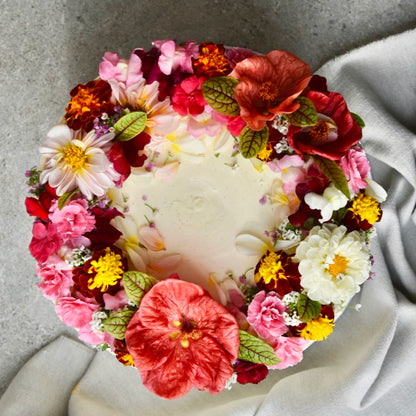 A cake decorated with many different shades of pink edible flowers is pictured from above 