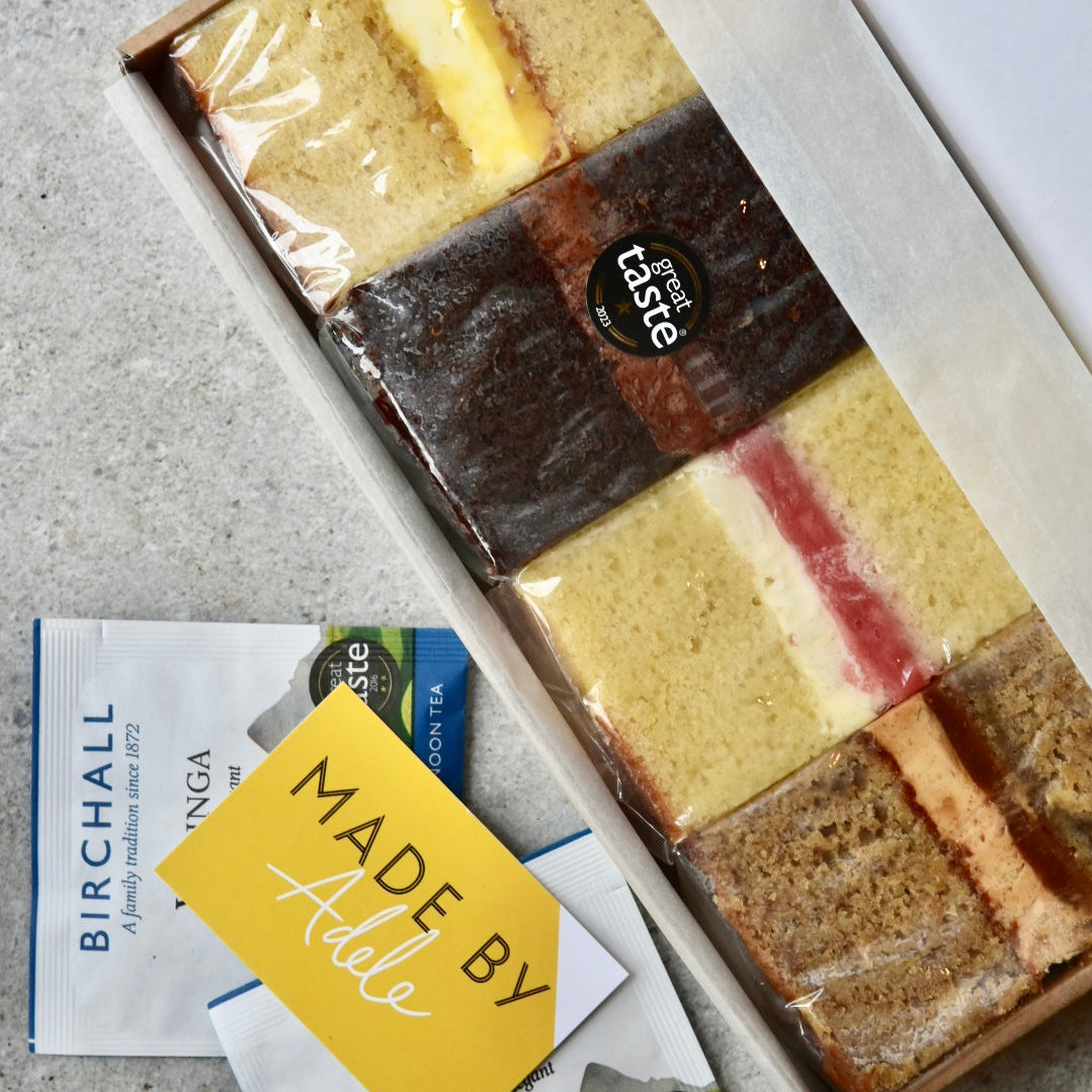 Four cakes placed in a postal box with Made By Adele's business car and a packet of Birchall's tea.