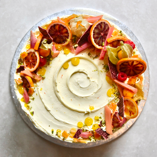 An overhead shot of a rhubarb flavoured cake decorated in vibrant reds and oranges natural flower and fruits.